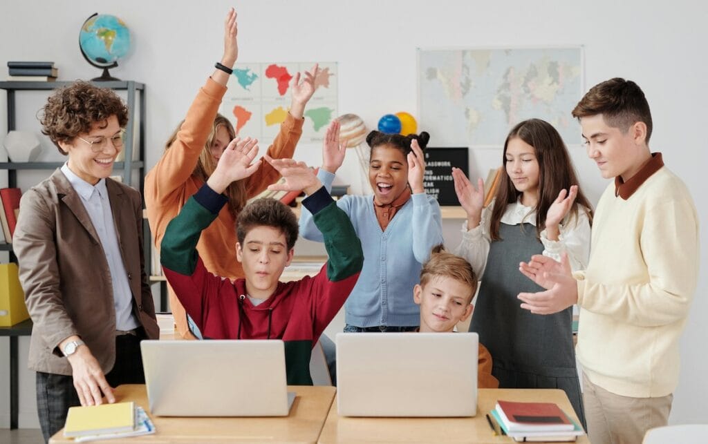 Students celebrating while learning on laptops, showing renewed engagement in the classroom post-pandemic.