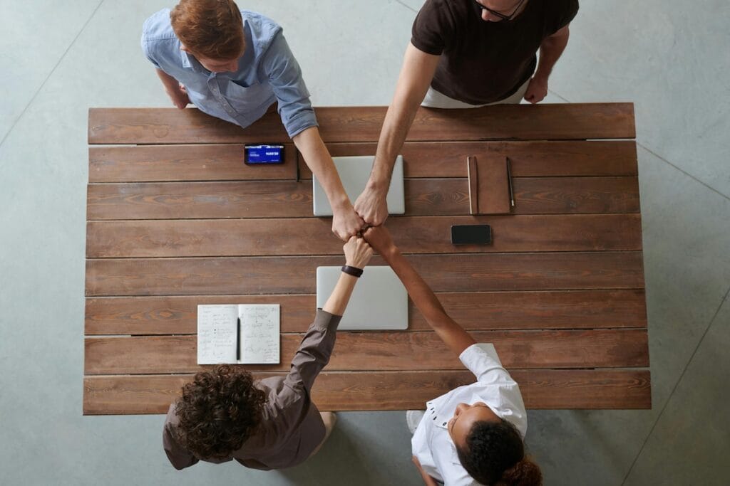 Teamwork: four people fist bumping over table.