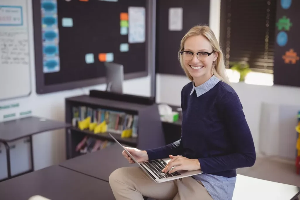 Smiling teacher using laptop in classroom