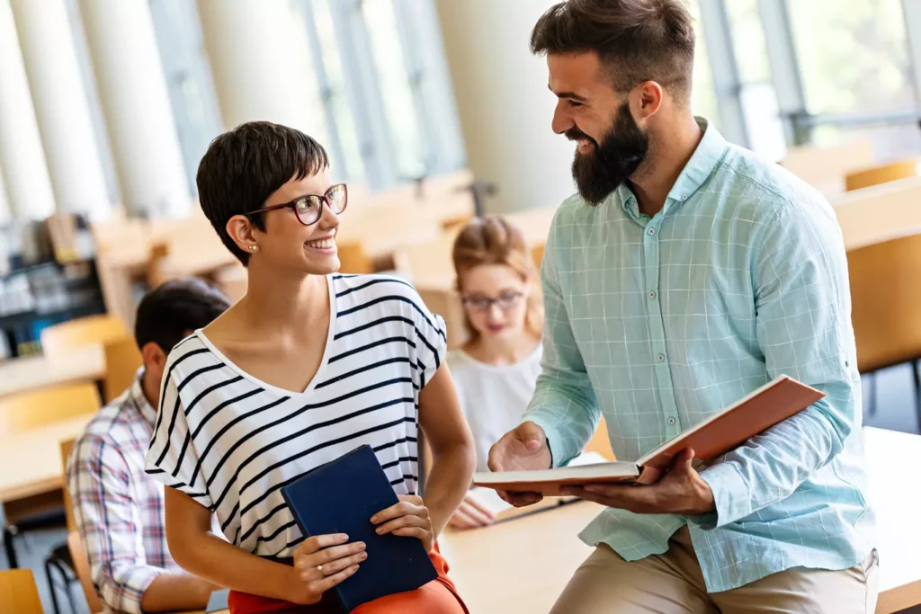 Two smiling students talk in a bright classroom.