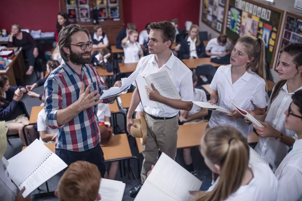 Teacher discusses scripts with students in a crowded classroom.